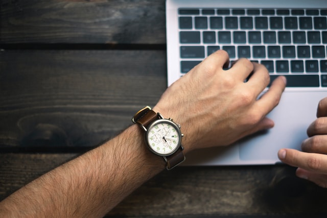 person wearing a brown watch with their left hand resting on an open laptop