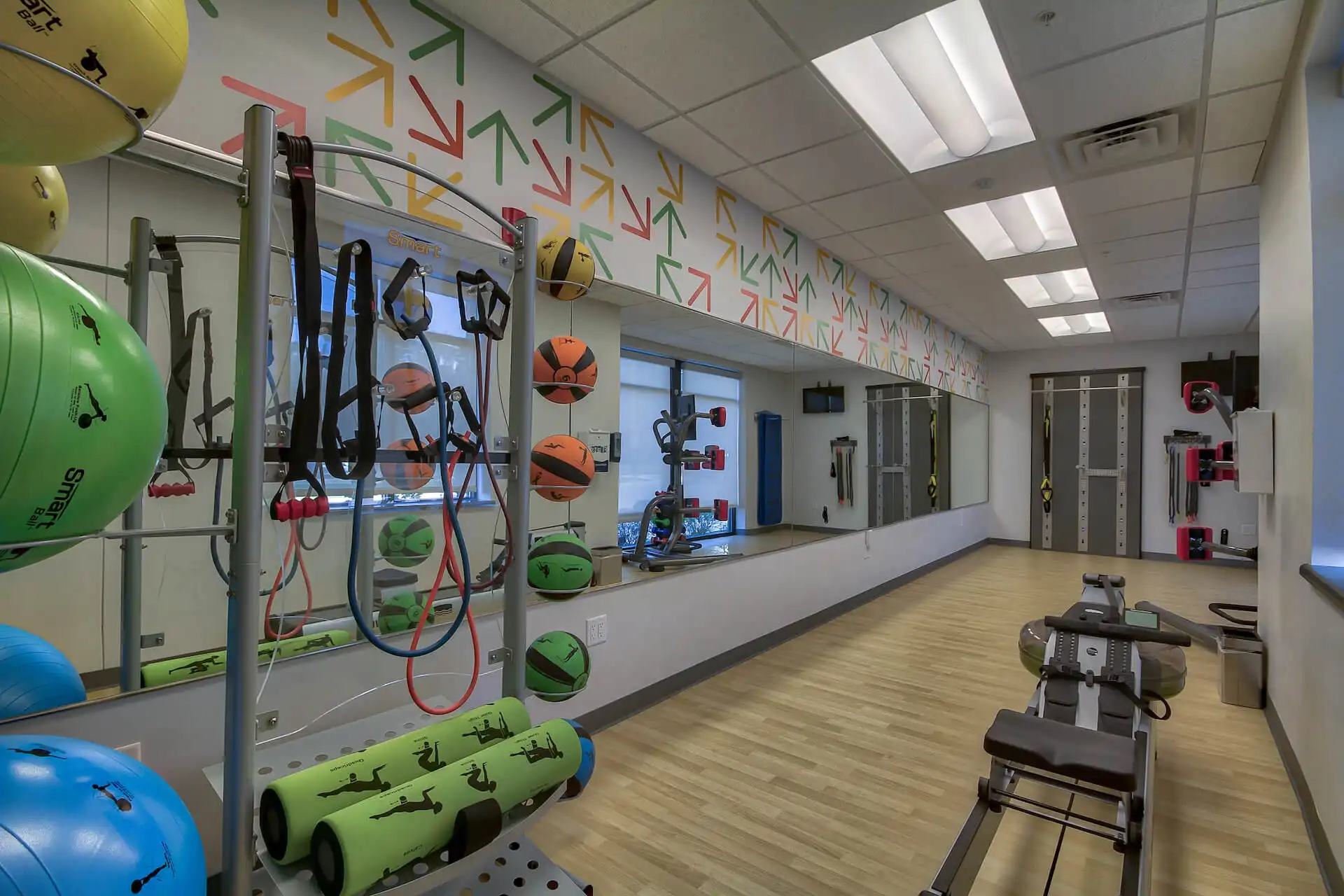 fitness center with wall length mirror, rowing machine, resistance bands, rollers, medicine balls, and balance balls.